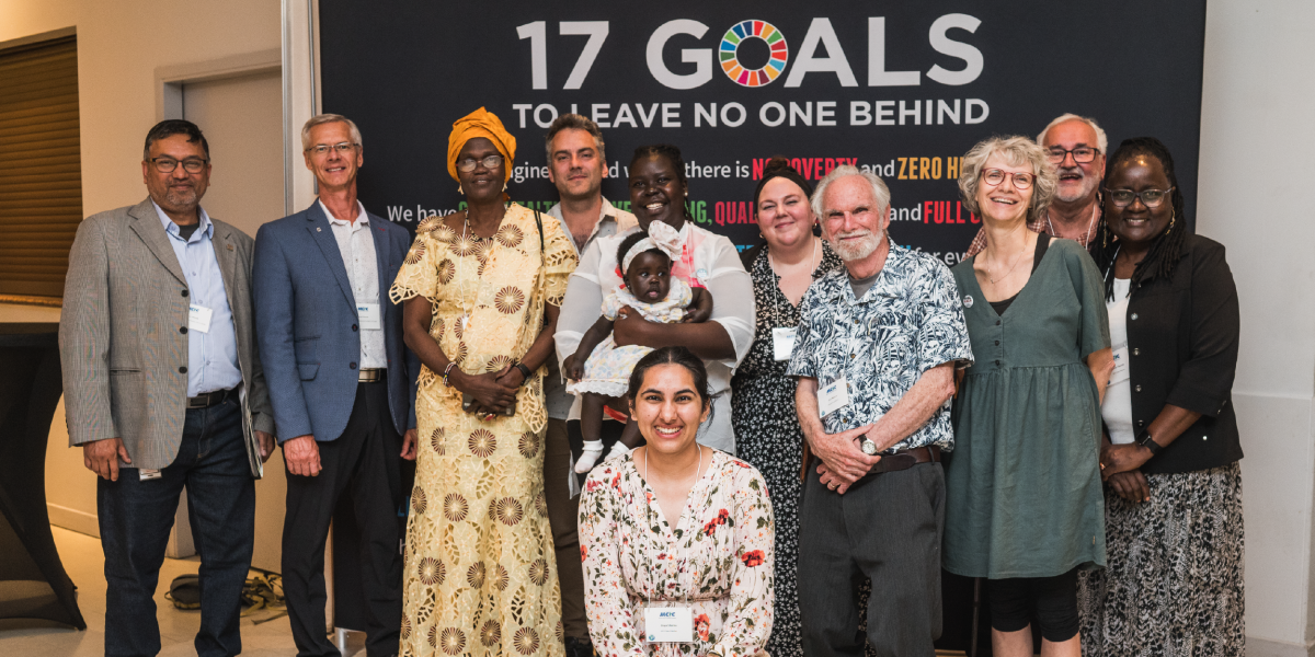 A group of people stand in front of a black background reading the 17 Goals